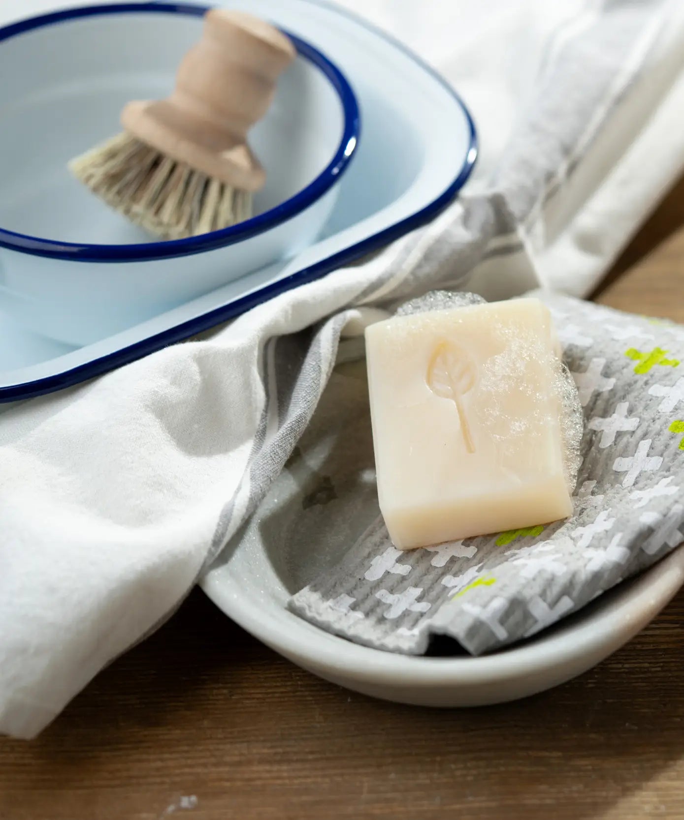 Lathered blossom breeze Ecoliving 100% vegan dish soap bar in a small bowl with a kitchen items in the background.