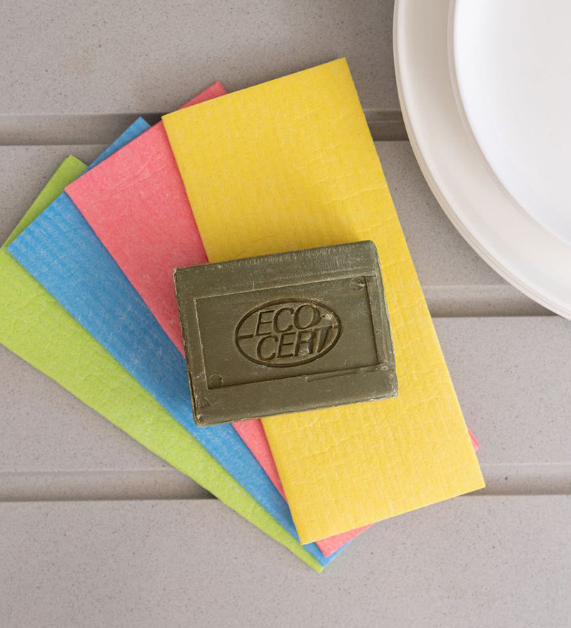 A bar of Ecoliving Organic Marseille Household Soap Bar placed on a pile of ecoliving compostable sponge cloths. 