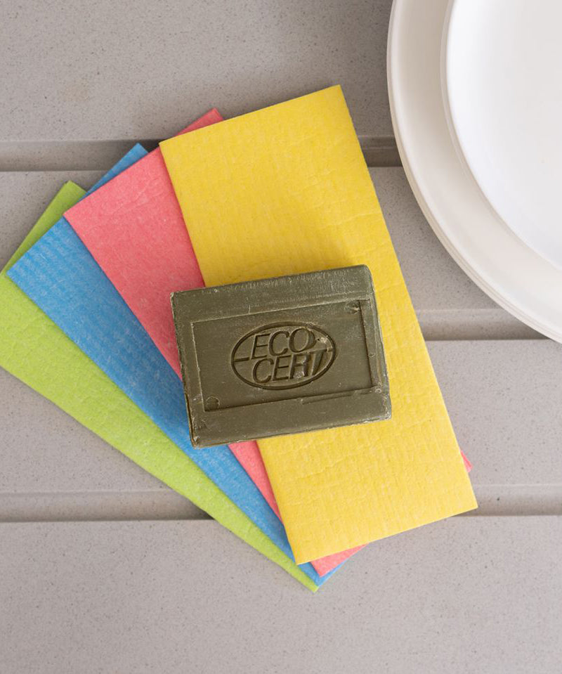 A bar of Ecoliving Organic Marseille Household Soap Bar placed on a pile of ecoliving compostable sponge cloths. 