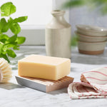 Ecoliving beech wood soap dish with a cream soap on top on a grey marble work top next to a tea towel and a green plant