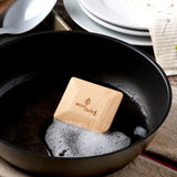 An EcoLiving wooden pot scraper shown in a black pot with soap suds.