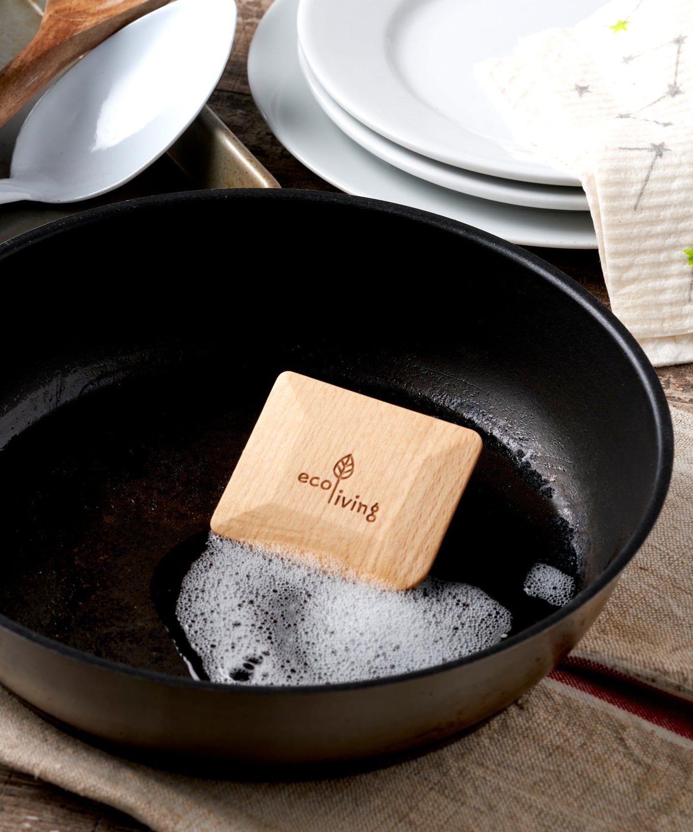 An EcoLiving wooden pot scraper shown in a black pot with soap suds.