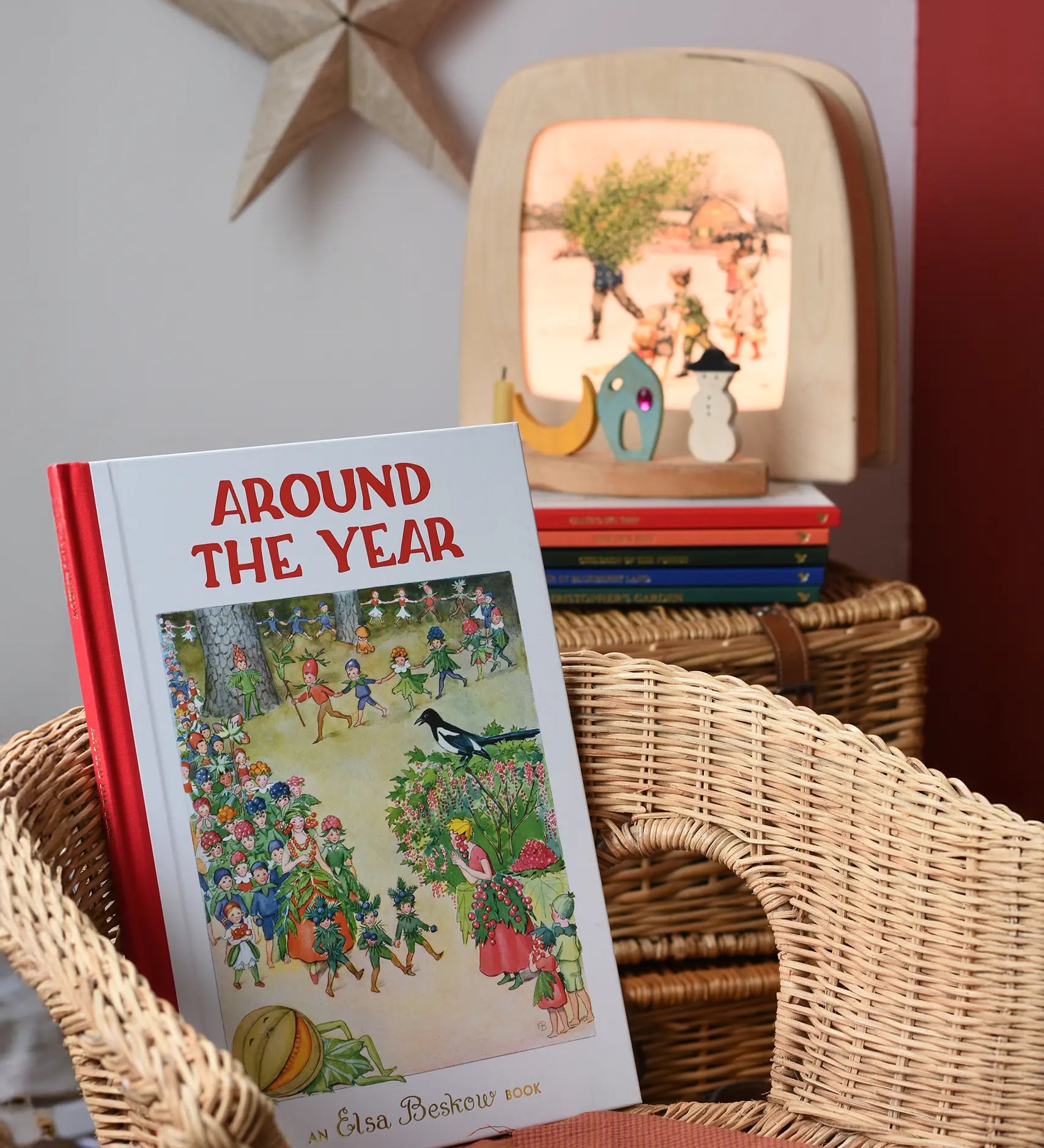 Around The Year children's hardback book by Elsa Beskow placed on a child's wicker chair with a Toverlux lamp with December artwork displayed in the background with a decorated celebration ring.