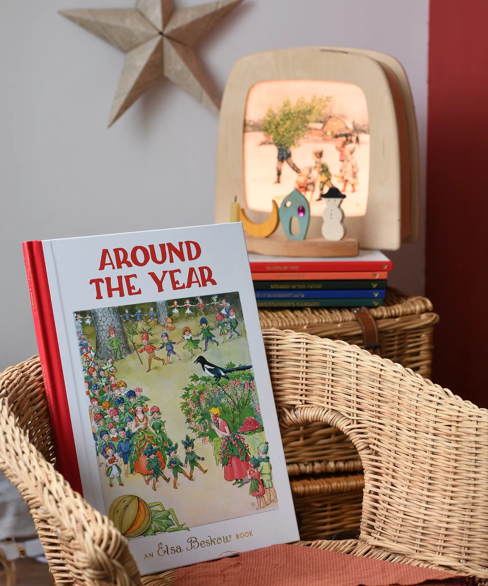 Around The Year children's hardback book by Elsa Beskow placed on a child's wicker chair with a Toverlux lamp with December artwork displayed in the background with a decorated celebration ring.