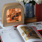 Around The Year children's hardback book by Elsa Beskow shown open on the November page with a Toverlux lamp with November artwork displayed in the background.