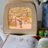 Around The Year children's hardback book by Elsa Beskow shown open on the September page with a Toverlux lamp with September artwork displayed in the background.