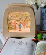 Around The Year children's hardback book by Elsa Beskow shown open on the September page with a Toverlux lamp with September artwork displayed in the background.