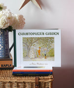 Christopher's garden children's hardback book by Elsa Beskow placed on a wicker hamper on a stack of other Elss Beskow books.