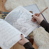 Inside page from the The World of Elsa Beskow: A Vintage Colouring Book. An adult's hand can be seen holding the book and a colouring pencil. Black and white line art coloring page illustration.