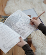 Inside page from the The World of Elsa Beskow: A Vintage Colouring Book. An adult's hand can be seen holding the book and a colouring pencil. Black and white line art coloring page illustration.