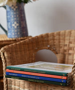 Stack of Elsa Beskow hardback children's books placed on a child's wicker chair. 