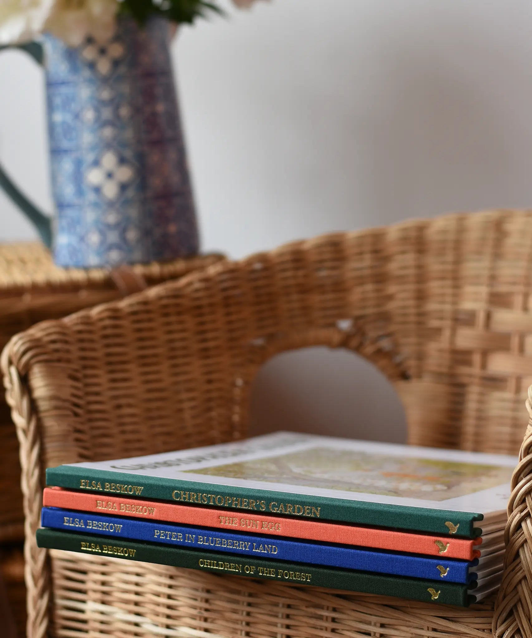 Stack of Elsa Beskow hardback children's books placed on a child's wicker chair. 