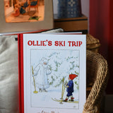 Ollie's Ski Trip by Elsa Beskow hardback children's book placed on a child's wicker chair with a Toverlux lamp in the background.