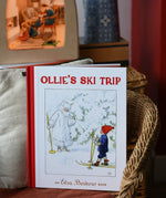 Ollie's Ski Trip by Elsa Beskow hardback children's book placed on a child's wicker chair with a Toverlux lamp in the background.