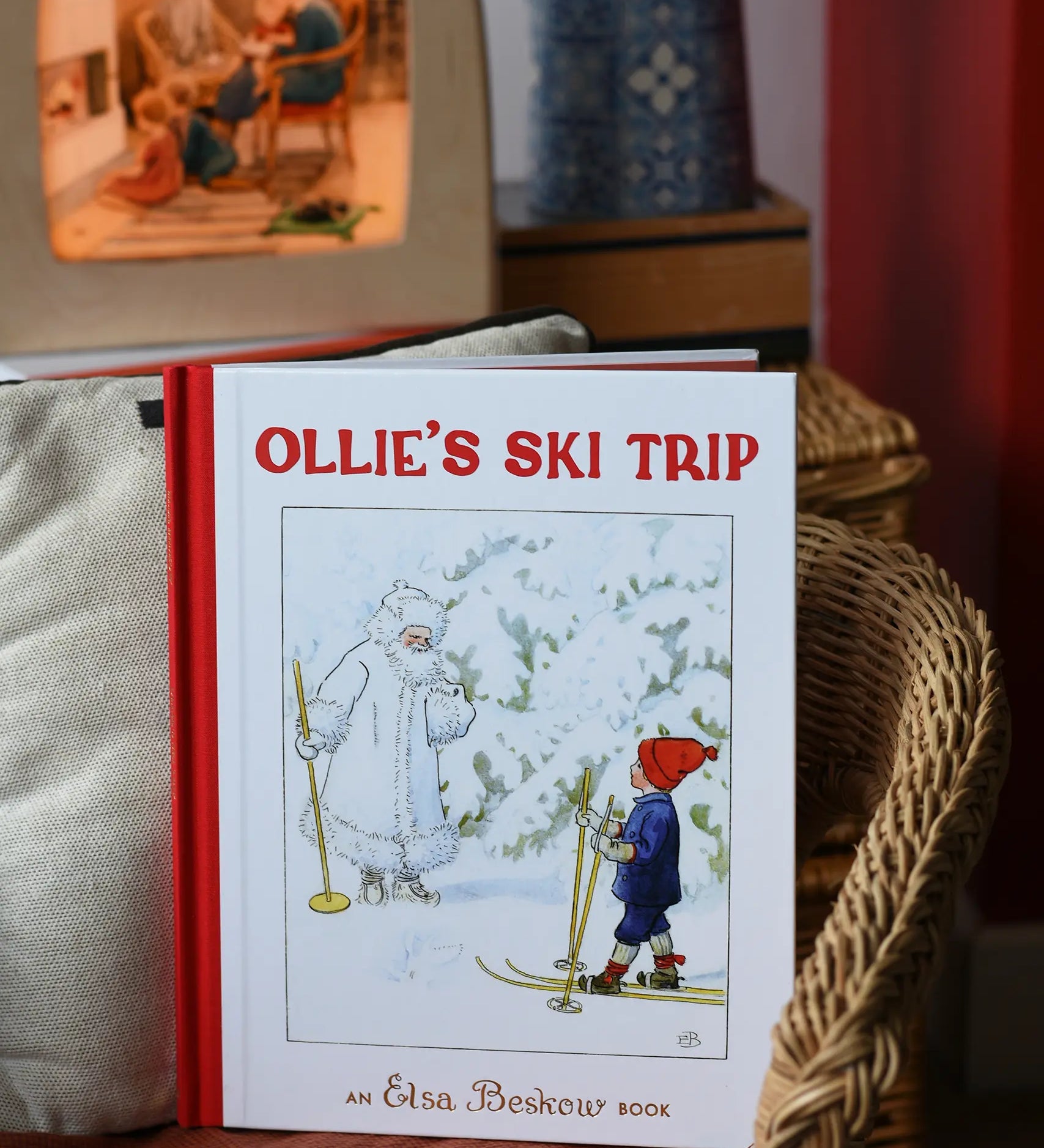 Ollie's Ski Trip by Elsa Beskow hardback children's book placed on a child's wicker chair with a Toverlux lamp in the background.