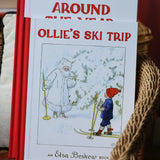 Ollie's Ski Trip by Elsa Beskow hardback children's book placed on a child's wicker chair with the around the year book placed behind it.