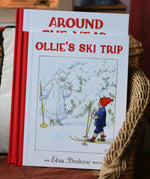 Ollie's Ski Trip by Elsa Beskow hardback children's book placed on a child's wicker chair with the around the year book placed behind it.
