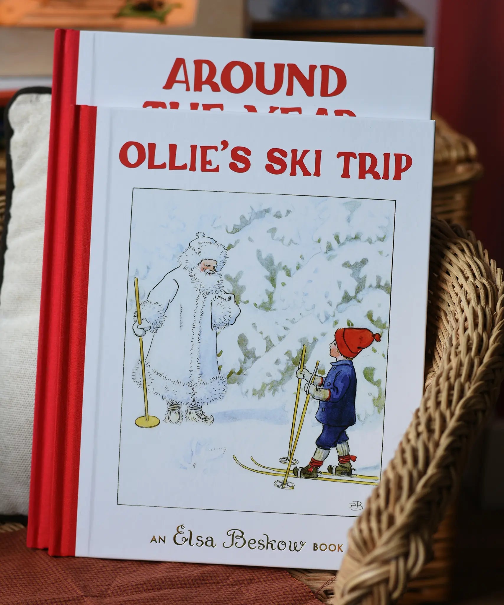 Ollie's Ski Trip by Elsa Beskow hardback children's book placed on a child's wicker chair with the around the year book placed behind it.