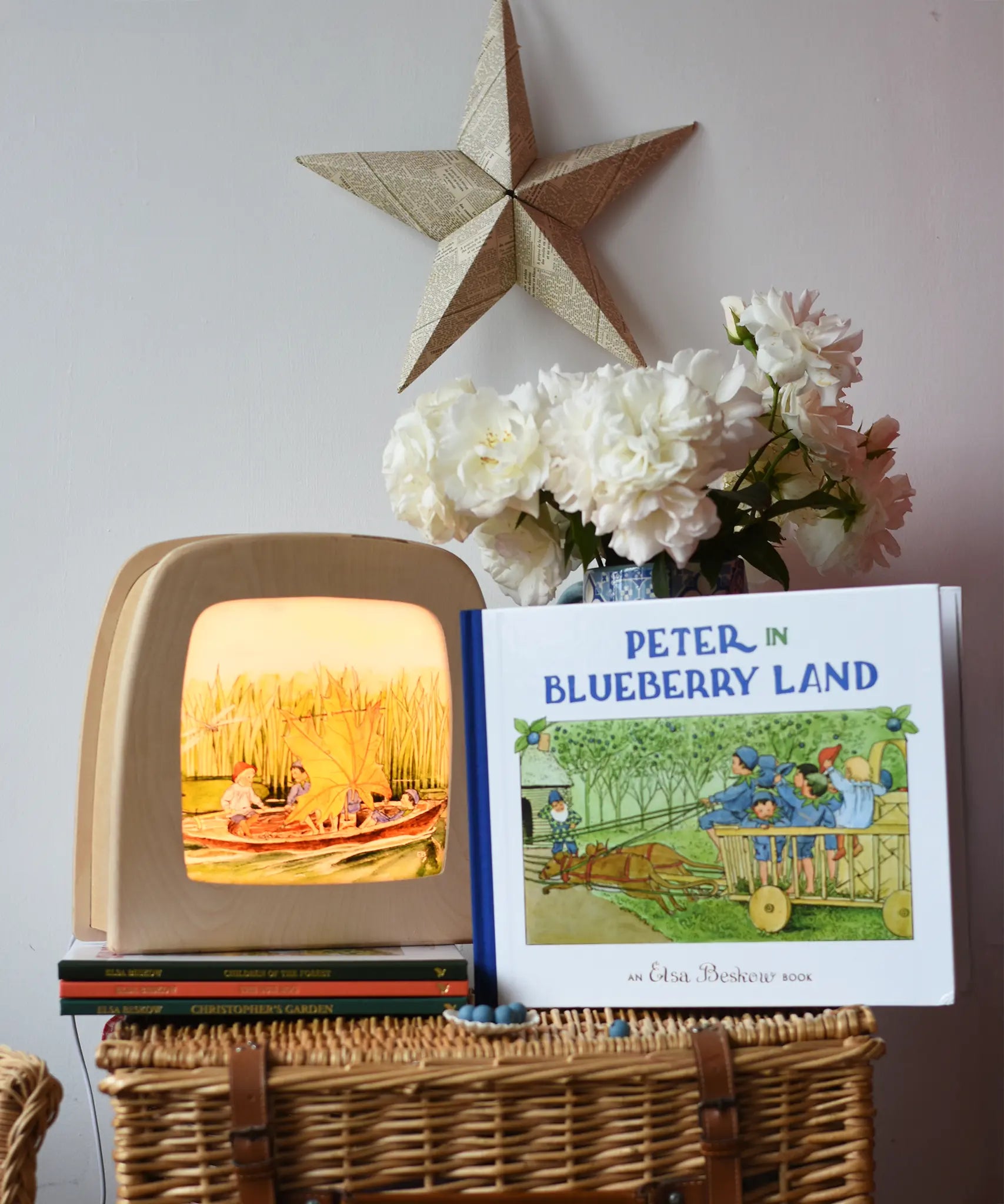 Peter in Blueberry Land children's hardback book by Elsa Beskow placed on a wicker hamper next to a Toverlux lamp with coordinating artwork.