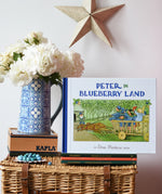 Peter in Blueberry Land children's hardback book by Elsa Beskow placed on a stack of book on a wicker hamper