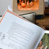 Close up of a page from the The sun egg children's hardback book by Elsa Beskow with a Toverlux lamp with sun egg art work displayed inside in the background.