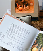 Close up of a page from the The sun egg children's hardback book by Elsa Beskow with a Toverlux lamp with sun egg art work displayed inside in the background.