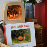 The sun egg children's hardback book by Elsa Beskow placed on a child's wicker chair with a Toverlux lamp with sun egg art work displayed inside.