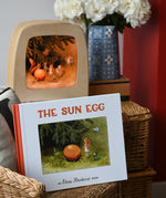 The sun egg children's hardback book by Elsa Beskow placed on a child's wicker chair with a Toverlux lamp with sun egg art work displayed inside.