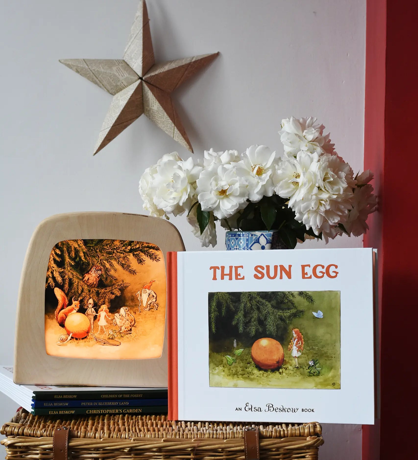 The sun egg children's hardback book by Elsa Beskow placed on a wicker hamper with a Toverlux lamp with sun egg art work displayed inside.