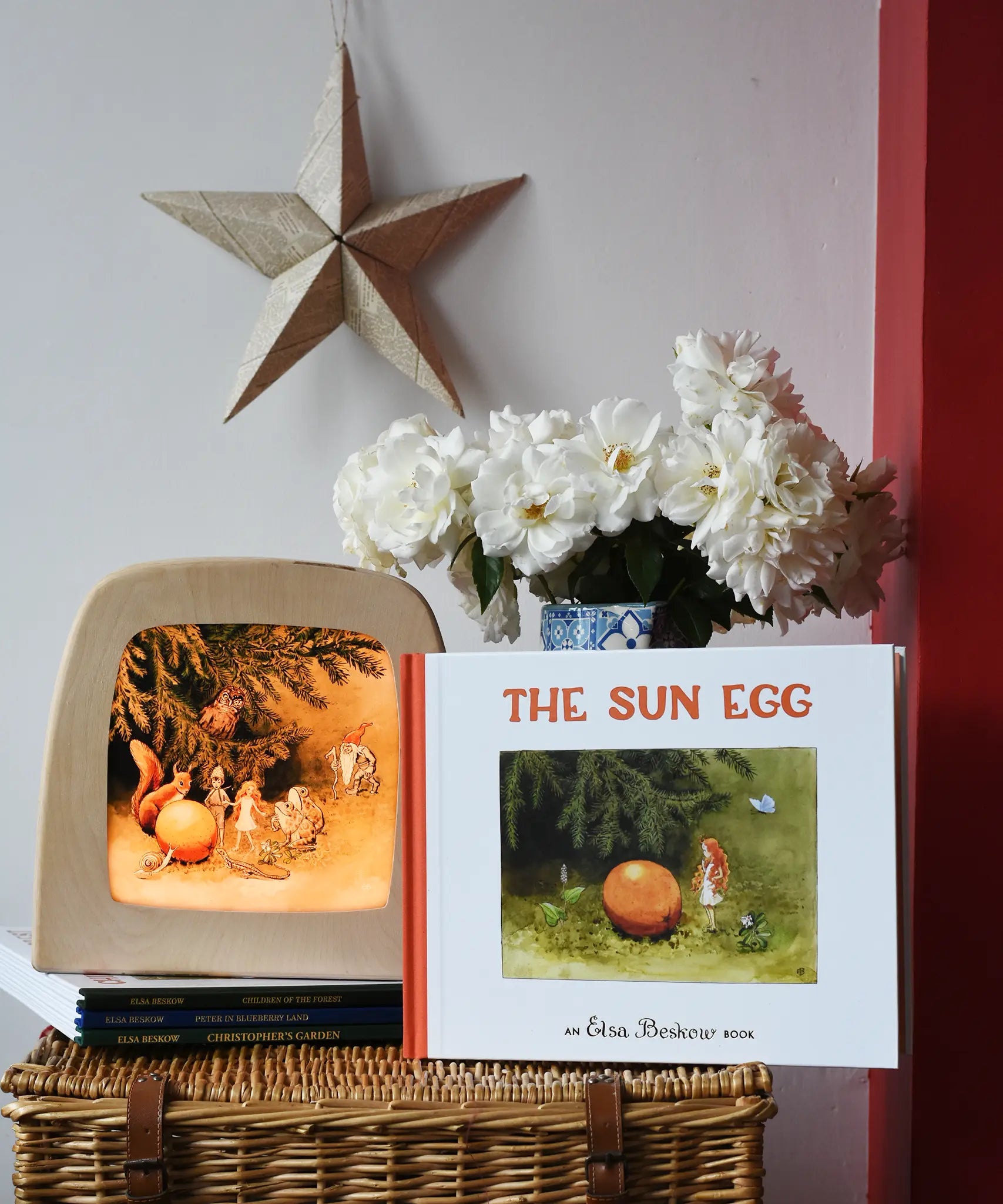 The sun egg children's hardback book by Elsa Beskow placed on a wicker hamper with a Toverlux lamp with sun egg art work displayed inside.