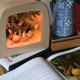The sun egg children's hardback book by Elsa Beskow shown open placed on a wicker hamper with a Toverlux lamp with sun egg art work displayed inside.