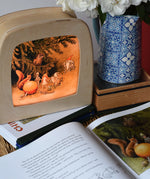 The sun egg children's hardback book by Elsa Beskow shown open placed on a wicker hamper with a Toverlux lamp with sun egg art work displayed inside.