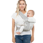 Woman with wavy blonde hair and a white t-shirt wearing her baby on her hip in the Ergobaby Adapt  SoftFlex™ Mesh Baby Carrier in Pearl Grey. Front view, white background. 