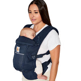 Woman with straight brown hair and a white t-shirt wearing her baby in the Ergobaby Adapt  SoftFlex™ Mesh Baby Carrier in Midnight Blue. Front view, white background. 