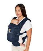 Woman with straight brown hair and a white t-shirt wearing her baby in the Ergobaby Adapt  SoftFlex™ Mesh Baby Carrier in Midnight Blue. Front view, white background. 