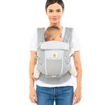 Woman with brown hair tied back and a white t-shirt wearing her baby in the Ergobaby Adapt  SoftFlex™ Mesh Baby Carrier in Pearl Grey. Front view, white background. 