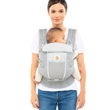 Woman with brown hair tied back and a white t-shirt wearing her baby in the Ergobaby Adapt  SoftFlex™ Mesh Baby Carrier in Pearl Grey. Front view, white background. 