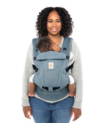 Woman with black curly hair and a grey jumper wearing her baby in the Ergobaby Adapt  SoftFlex™ Mesh Baby Carrier in Slate Blue. Front view, white background. 