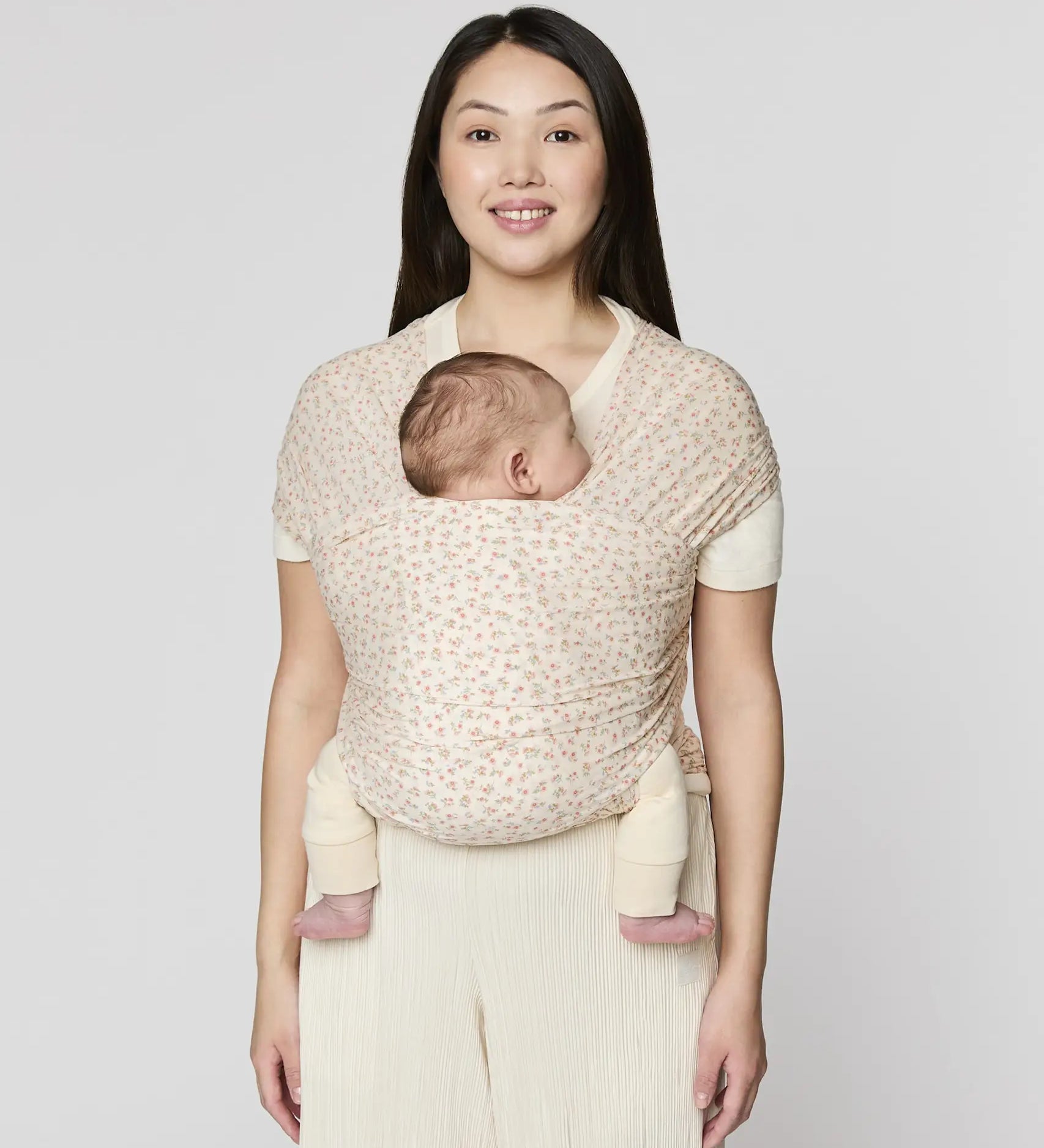 Mother carrying a baby in the Ergobaby aura sustainably knitted wrap carrier in dainty blooms in the frontal position