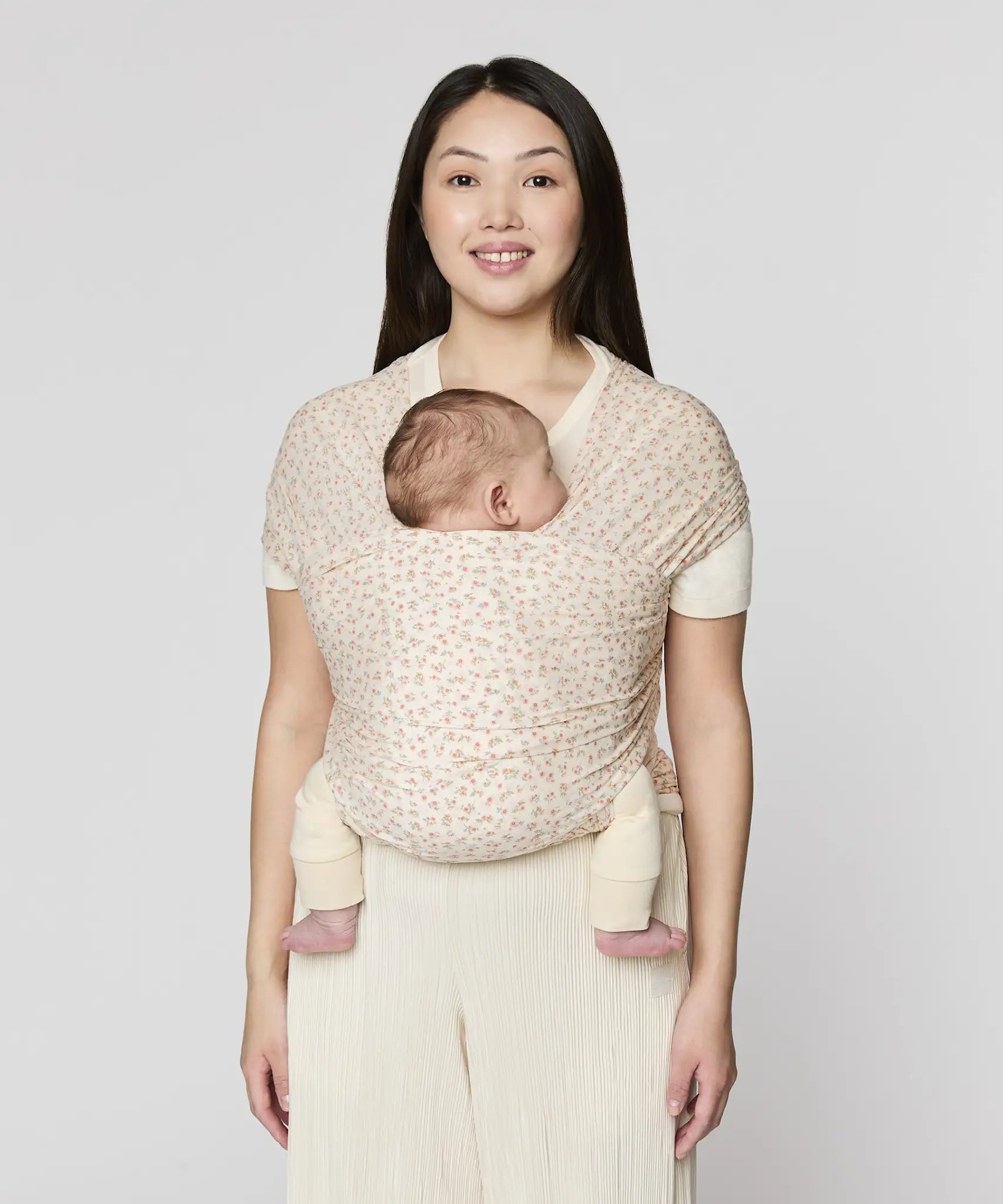 Mother carrying a baby in the Ergobaby aura sustainably knitted wrap carrier in dainty blooms in the frontal position