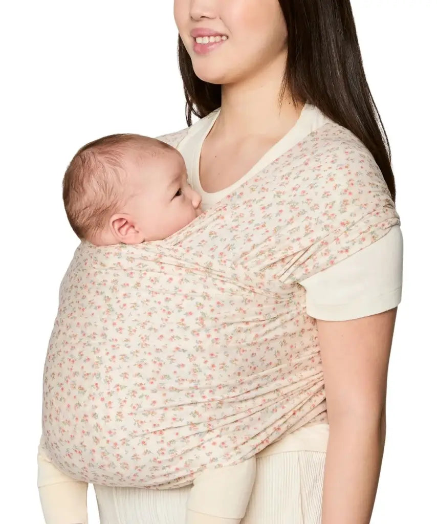 Side of mother carrying a baby in the Ergobaby aura sustainably knitted wrap carrier in dainty blooms in the frontal position