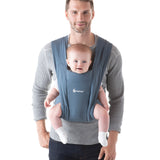 Man wearing a grey jumper and his baby on his front facing outwards in the Ergobaby Embrace Soft Knit Newborn Baby Carrier in Oxford Blue. Front view white background.