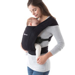 Woman wearing a grey top and her sleeping baby on her front in the Ergobaby Embrace Soft Knit Newborn Baby Carrier in Pure Black. Side view white background.