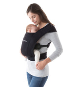 Woman wearing a grey top and her sleeping baby on her front in the Ergobaby Embrace Soft Knit Newborn Baby Carrier in Pure Black. Side view white background.