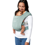 Woman wearing a white top and her baby on her front facing inwards in the Ergobaby Embrace Soft Knit Newborn Baby Carrier in Jade. Side view white background.