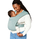 Woman wearing a white top and her baby on her front facing inwards in the Ergobaby Embrace Soft Knit Newborn Baby Carrier in Jade. Side view white background.
