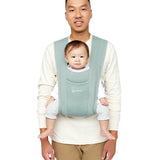 Man wearing a white top and his baby on his front facing outwards in the Ergobaby Embrace Soft Knit Newborn Baby Carrier in Oxford Blue. Front view white background.