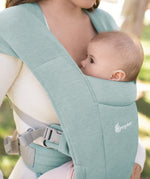 Close up of a baby facing inwards in the Ergobaby Embrace Soft Knit Newborn Baby Carrier in Jade. Side view garden background.