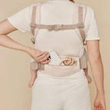 A woman wearing the Ergobaby Omni Deluxe Cotton baby carrier in Natural Beige showing the pouch on the waist strap. 