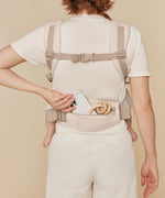 A woman wearing the Ergobaby Omni Deluxe Cotton baby carrier in Natural Beige showing the pouch on the waist strap. 
